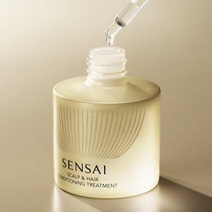 A clear droplet dropping from a dropper into a hair treatment bottle illuminated in gold
