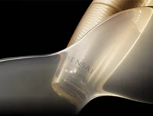  Goldener Glasflakon, teilweise mit einem transparenten goldenen Schleier bedeckt, vor einem schwarzem Hintergrund