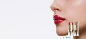 Quatre rouges à lèvres de teintes variées sont alignés dans des boîtiers dorés devant un gros plan de lèvres rouges et brillantes