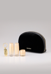 Una pochette nera con chiusura a zip, con un set di 3 campioni mini-taglie di prodotti skincare e un ciondolo su una superficie di marmo nero.