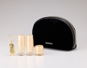 Una pochette nera con chiusura a zip, con un set di 3 campioni mini-taglie di prodotti skincare e un ciondolo su una superficie di marmo nero.