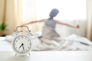 little boy sitting and stretching in bed at home in the morning on a window background with alarm clock