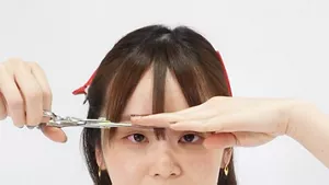眉間部分の前髪を額の近くで指にはさみ、刃先で切る画像
