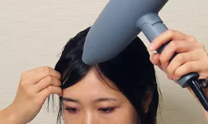 前髪を手ぐしで整えながら、ドライヤーの温風を当てる画像