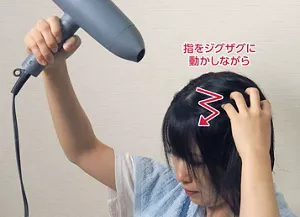頭を少し下に傾け、指をジグザグに動かしながら根元にドライヤーの風を当てる画像