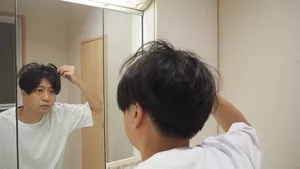 鏡の前で、短い髪の乾き具合を手で確かめる男性の画像