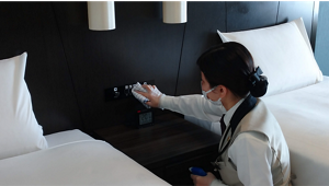 客室でベッド脇のボタンパネルを清掃する従業員の写真