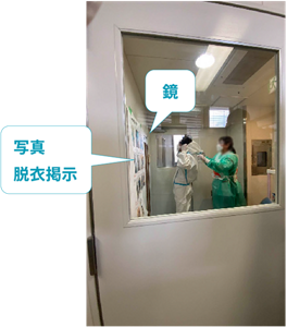 感染症対応訓練で個人防護具の脱衣手順を掲示している様子。鏡の横に脱衣手順ポスターを貼り、医療従事者が正しい手順を確認しながら訓練している。