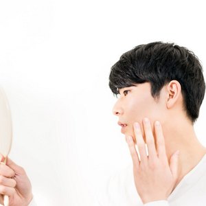 手鏡で左頬の肌の状態を確認している男性