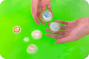 緑のお湯にペットボトルのキャップが入っている氷を浮かべて遊んでいる画像