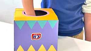 バブみくじの箱に手を入れて、引くバブを選んでいる画像