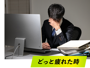 どっと疲れた時。オフィスで残業中、デスクワークしながら、かなり疲れている様子の男性社員イメージ