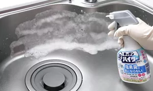 シンクに向かってキッチン泡ハイター無臭性タイプをスプレーしている写真。