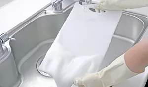 まな板にスプレーされたキッチン泡ハイターの泡を洗い流している写真。流し終えた箇所はきれいに漂白されている。