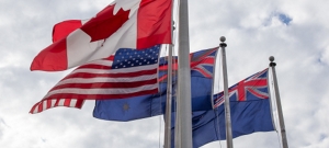 The Canadian, United States, Australian and New Zealand flags blowing in the wind on a cloudy day.
