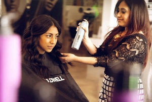 A young, female hair stylist in a salon holding a bottle of hair spray, finishing a customer's hair.