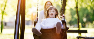 A young girl with Down syndrome being pushed on a swing by an out-of-focus person in the background.