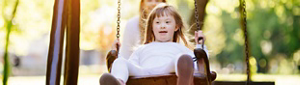 A young girl with Down syndrome being pushed on a swing by an out-of-focus person in the background.