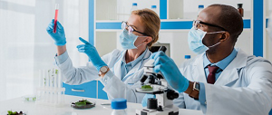 A woman and a man in a lab wearing personal protective equipment. They are looking at a test tube that the woman is holding.