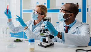 A woman and a man in a lab wearing personal protective equipment. They are looking at a test tube that the woman is holding.