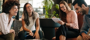 Four young, diverse co-workers in a modern environment laughing.