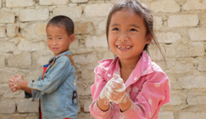 Two young children, one boy and one girl, washing their hands.