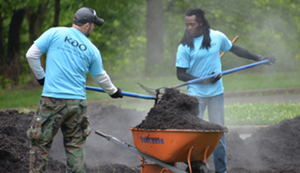 Two male KAO employees at a volunteer event wearing bright blue shirts and shoveling mulch.