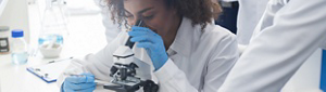 A young, female, Black scientist looking through a microscope.