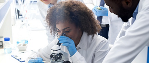 A young, female, Black scientist looking through a microscope.