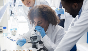 A young, female, Black scientist looking through a microscope.