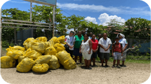 A group of people standing outside next to a large pile of garbage collected in yellow waste bags. 