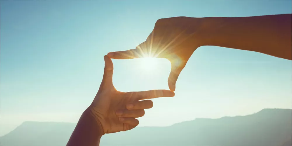 An image of hands framing the sun, symbolizing a new perspective and a positive vision for the future