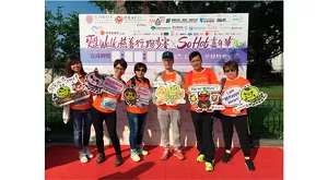 6名花王香港員工穿著活動專屬的橙色T-shirt，拿著印有活動標語的卡通道具，在「甦Walk慈善行・跑步賽 X So HOT嘉年華」背景板前合照。