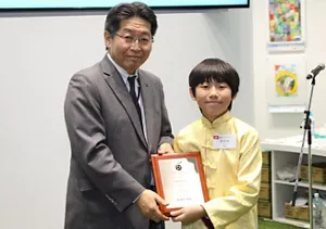 一個身穿淡黃色民族服裝的小朋友從評委手上接過獎狀。