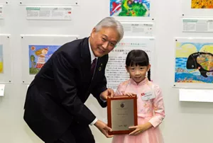 一個身穿粉紅色民族服裝的小女孩從時任花王株式會社總裁兼執行長澤田道隆先生手上接過獎狀。