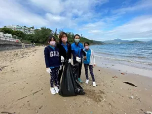 兩名花王香港員工和他們的家人在海灘上提著袋子清理垃圾。