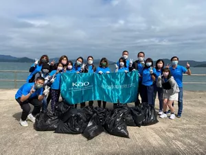 一群參加者舉著印有花王標誌的藍色橫額在岸邊與收集到的十數袋海灘垃圾合照。