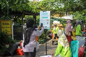 Photo of a woman scanning an information board for the Sorting and Collecting Waste activity of the Kao BERGERAK BISA Program