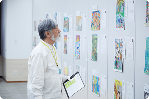 白い手袋をつけた審査員が壁に展示されたこどもたちの作品を真剣に見て審査をしている様子
