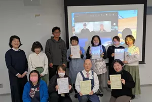 贈呈式の会場とオンライン先をつないで、助成先の代表の皆様と事務局が記念撮影をしている様子