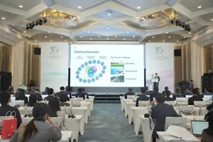Photograph of a business conference presentation, with seated attendees facing a large projection screen labeled “Chemical Business.” Slide displays a circular chemical-sector diagram, blue-green process or product nodes, and “Key Focus in Vietnam” panels for agriculture, semiconductor, and infrastructure.