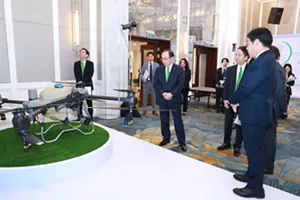 Photograph shows officials in suits viewing a large unmanned aerial vehicle displayed on artificial grass inside an elegant exhibition hall.