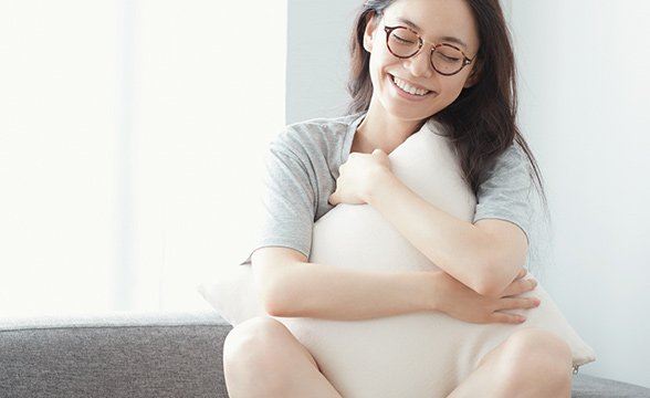 Young happy woman with smooth skin cuddling pillow