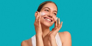 Smiling woman applying gentle skincare products to her face
