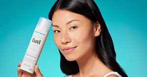 Woman holding a can of moisturising spray against a teal background