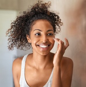 Happy woman applying dabs of moisturiser to her under eye area