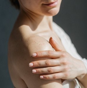 Woman gently applying moisturiser to her shoulder