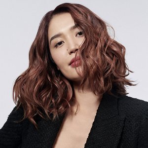 一位擁有美麗長髮的紅髮女性在灰色的背景前使用Goldwell頭髮產品。