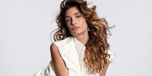 white woman with long brown hair which leans forward in front of a clean grey background looking into the camera