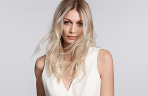 white woman with long blonde hair which stands in front of a clean grey background looking into the camera